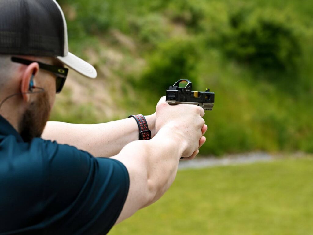 Man wearing PPE at outdoor shooting range is zeroing his red dot sight