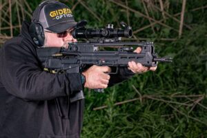 Man wearing a Gideon Optics hat and protective ear and eyewear aiming his firearm with a Guardian LPVO mounted