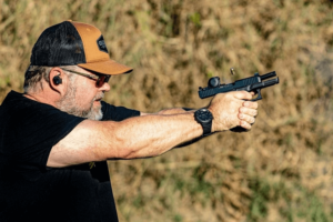 Man wearing protective eye and earwear shooting a firearm with an optic mounted at an outdoor range - Gideon Optics Man wearing protective eye and earwear shooting a firearm with an optic mounted at an outdoor range