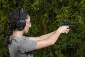 Woman firing a pistol with a Gideon Optics Mediator red dot sight mounted while at an outdoor shooting range