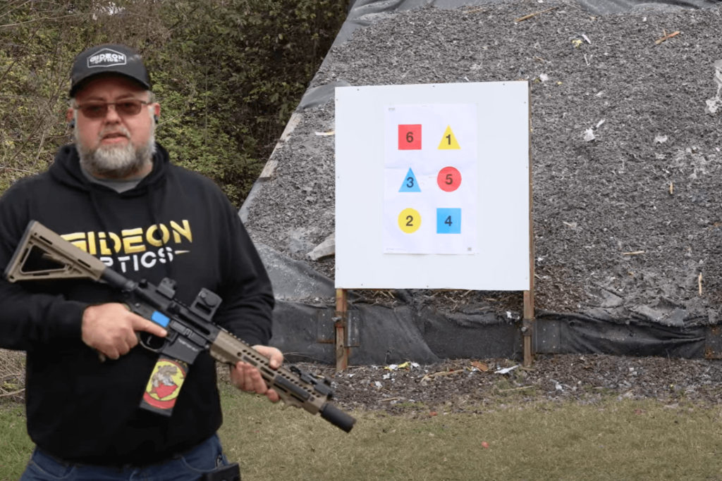 Mike from Gideon Optics holding a firearm at an outdoor shooting range as he stands in front of targets