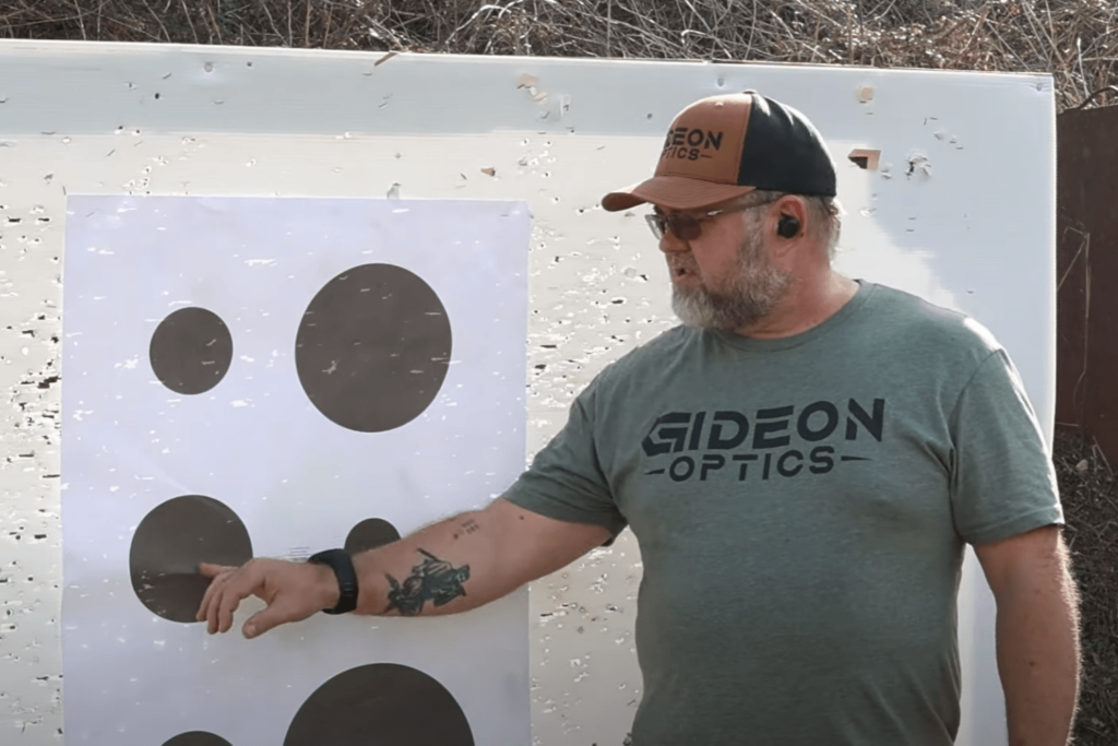 Man at an outdoor shooting range pointing at a target while giving a demonstration