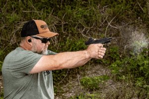 Man at an outdoor shooting range firing a pistol with a Valor Mini red dot mounted - Gideon Optics Man at an outdoor shooting range firing a pistol with a Valor Mini red dot mounted