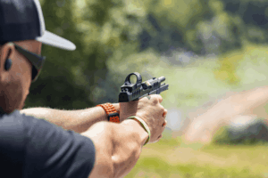 Man at an outdoor shooting range firing his pistol while practicing self defense drills - Gideon Optics Man at an outdoor shooting range firing his pistol while practicing self defense drills