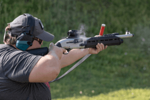 Man firing a shotgun with a Gideon Optics red dot mounted at an outdoor shooting range - Gideon Optics Man firing a shotgun with a Gideon Optics red dot mounted at an outdoor shooting range