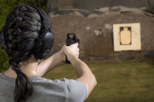 woman aiming a pistol with a red dot mounted towards a target at an outdoor shooting range - Gideon Optics woman aiming a pistol with a red dot mounted towards a target at an outdoor shooting range