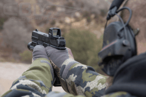 Behind the back view of a man wearing camo winter gear firing a pistol with a Gideon Optics red dot mounted