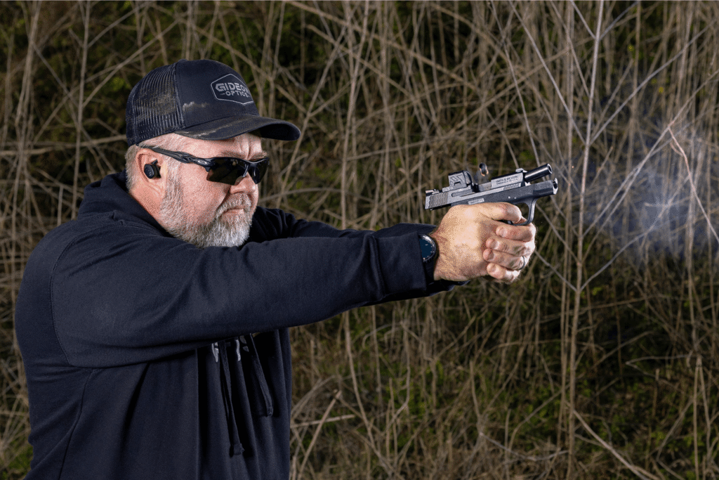 Man wearing all black is firing a pistol with a micro red dot mounted