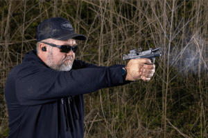 Man wearing all black is firing a pistol with a micro red dot mounted