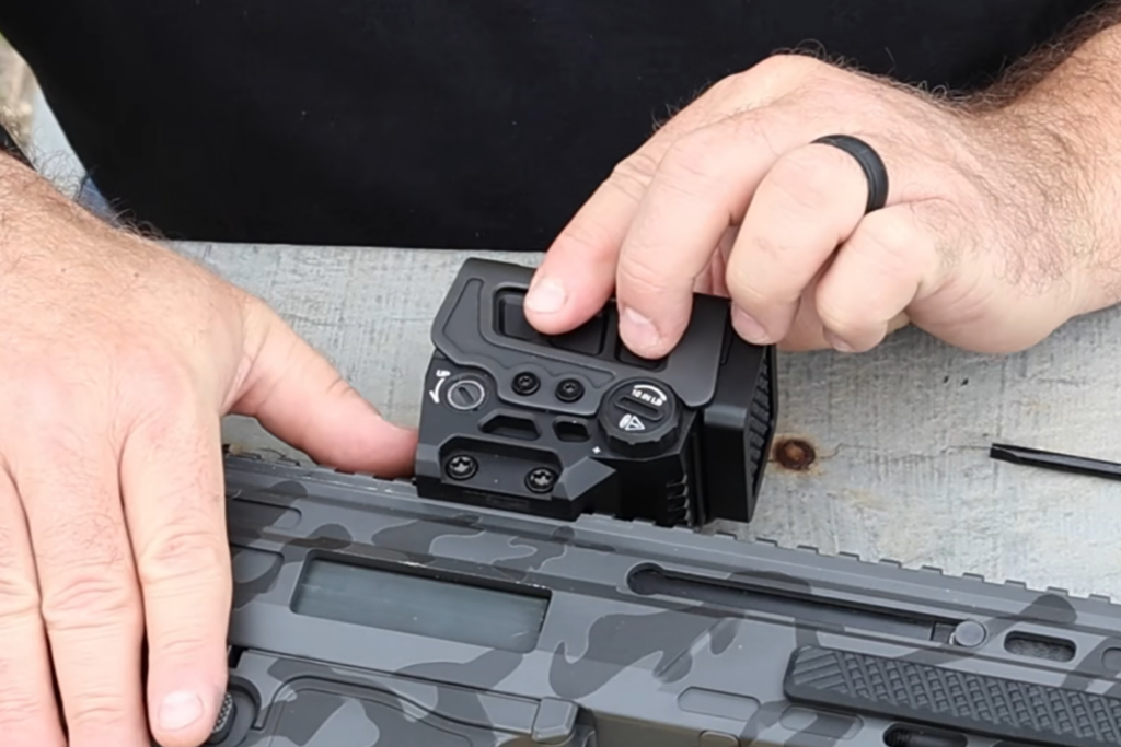 image - Gideon Optics one hand holding a rifle and the other hand holding a new optic up to mount